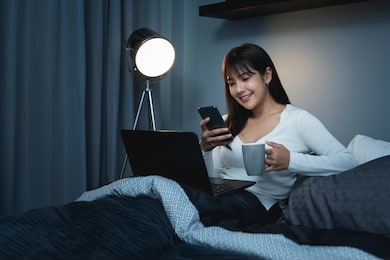 asian women using the smart phone and working on laptop on the bed before she sleeping at night.