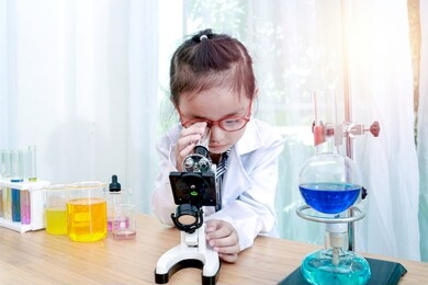 little asian girl doing experiments in laboratory. cool kid studying biology science , child pretending to be microbiologist and has fun in lab. young scientist with microscope.