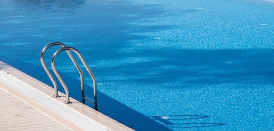 banner. the pool with bright blue water and a metal staircase in the hotel.