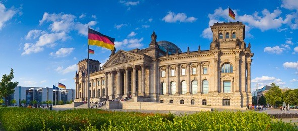 warm evening sunlight illuminating the mighty reichstag parliament (1894) with clear blue sky and flags flying.