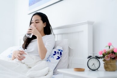 young asian woman drink water from a glass after wake up in the morning in a bedroom.