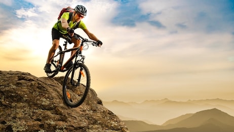 cyclist riding the bike down the rock at sunrise in the beautiful mountains on the background. extreme sport and enduro biking concept.