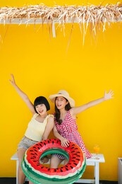 two asian women bestfriend closefriend on summer vacation. traveling together on the beach. over yellow background.