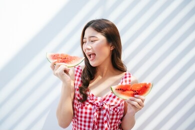 beautiful young asian woman on red dress holding piece of watermelon. pretty asian woman enjoy eating piece of watermelon. over white background.