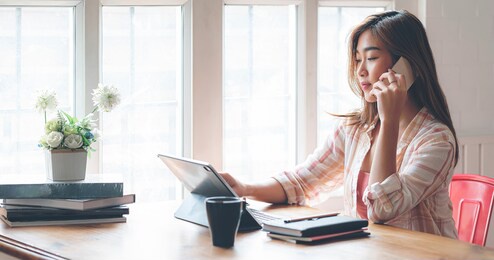 young beautiful asian woman using smartphone and working with laptop while sitting at office desk, working from home concept.