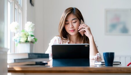 young beautiful asian woman using smartphone and working with laptop while sitting at office desk, working from home concept.