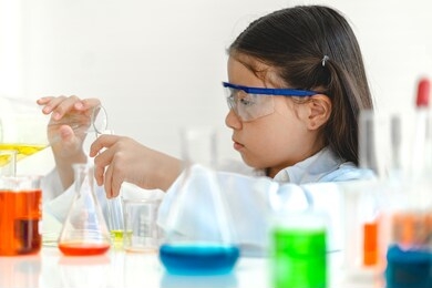cute little girl student child learning research and doing a chemical experiment while making analyzing and mixing liquid in glass at science class on the table.education and science concept