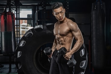 asian handsome man posting with dumbbells in dark gym
