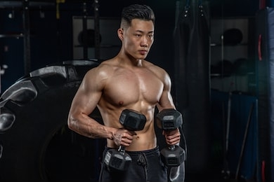 asian handsome man posting with dumbbells in dark gym