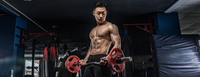 asian handsome man posting with dumbbells in dark gym