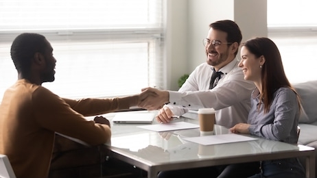 happy african american candidate shaking hands with businessman at job interview in office. businessman and businesswoman managers greeting client, good business partners negotiation.