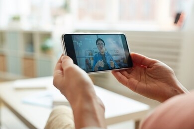 unrecognizable person watching asian man speaking while having online meeting on smartphone, horizontal close-up shot