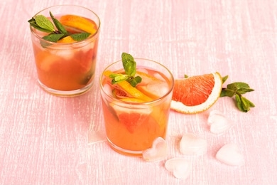 grapefruit cocktails with mint and ice. cold summer citrus fresh beverage on light pink wooden background