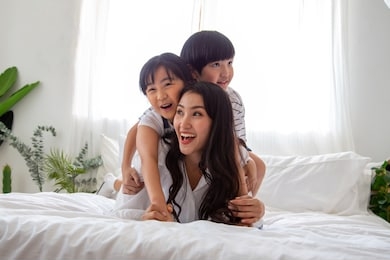 happiness of asian family with mom and son and daughter hug mother on white bed in bedroom, feeling happy and family relationship concept