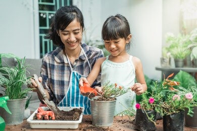 happy excited mother and her daughter gardening together plants some flower at home