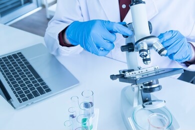 scientist, researcher, technician or student wear blue rubber gloves while using a microscope in a modern laboratory. education chemistry and science medical research concept.
