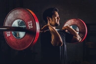 asian athletic strong man having workout and bodybuilding with barbells weightlifting front squat style in gym and fitness center in dark tone, selective focused