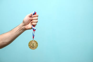 the male hand of the winning athlete holds the gold medal on a blue background space for text
