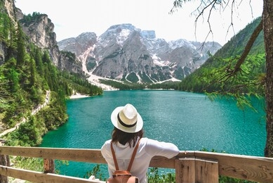 woman in straw hat with backpack standing and looking at lake in dolomites alps