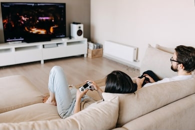 back view of a couple of man and woman playing video game on a console, sitting on couch in living room.