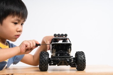 asian boy about 4 years old holding small screw screwdriver to fix car toy on white background