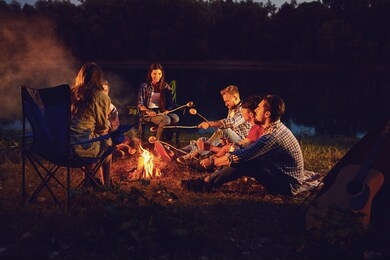 a group of people sitting by the bonfire next to the tent at night in the summer in autumn.
