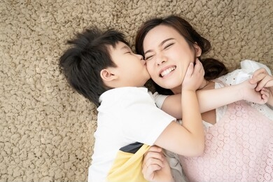 asian family mother and son happy kissing love together lying down on carpet floor, parent and kid is real people family.