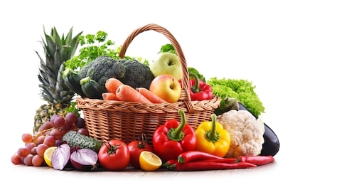 assorted organic vegetables and fruits in wicker basket isolated on white background.
