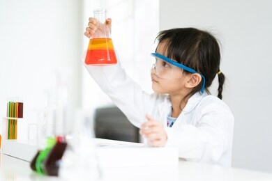 a little asian student is making experiment about the phase separation of oil and aqueous liquid in the flask at laboratory room, concept of chemical laboratory and science education for kid.