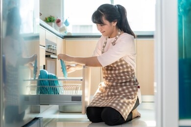 attractive young asian woman loading the dishwasher into cupboards at kitchen while doing cleaning at home during staying at home using free time about their daily housekeeping routine.

