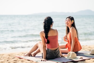 two lesbian asian traveler friend girls spending time together sit at beach in thailand. women smiling and laughing feeling fun with happiness enjoy traveling at beach and sea on holiday and vacation.