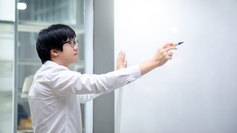 asian man teacher writing on blank whiteboard teaching lesson in classroom. male businessman presenting his project to coworkers in office conference room. education presentation or business meeting