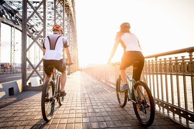 a man and a woman ride a bicycle towards the setting sun