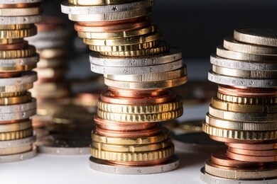 piled up coins, euros in different sizes leaning to the right on white surface and dark background