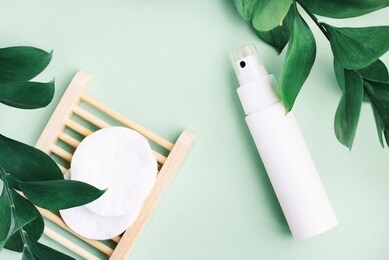 organic skin care and beauty treatment blue background. cosmetic product white spray bottle container, facial cleanser cotton pads, fresh plant leaves, top view pastel toned.