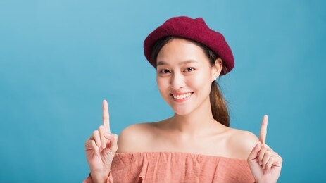 portrait of confident beautiful asian woman with hand pointing up and looking to camera isolated on blue colour background with studio shot.skincare for healthy face concept.