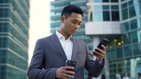 portrait shot of a young asian businessman, leading correspondence on the phone with coffee in his hands. financial business area.