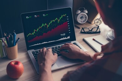 young casual asian business man looking checking trading prices on online stock market through laptop at home with graph showing on screen