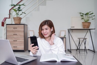 young asian business woman work from home and video conference via application on mobile phone,she 's smiling and show her hand for greeting with her colleagues