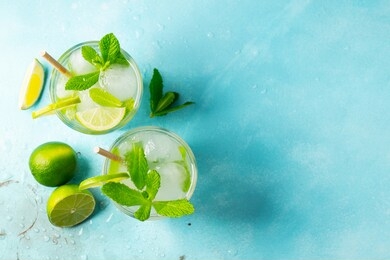 two homemade lemonade or mojito cocktail with lime, mint and ice cubes in a glass on a light stone table. fresh summer drink. top view with copy space