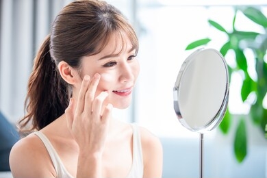 asian young woman look in mirror and apply moisturized cream or sunscreen on her face