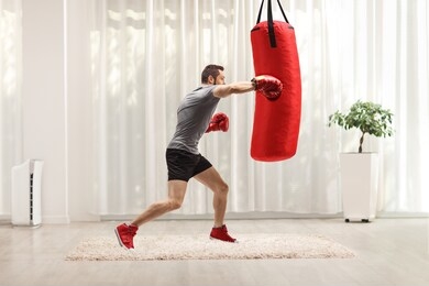 man exercising punching bag with boxing gloves at home