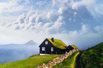 foggy morning view of a house with typical turf-top grass roof and blue cloudy sky in the velbastadur village on streymoy island, faroe islands, denmark. landscape photography