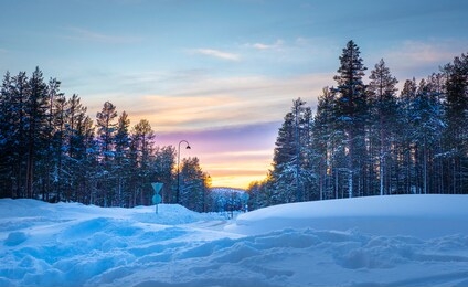 view of street with pine trees forest and mountain at sunset time with layer of colourful sky. at kittila, finland.