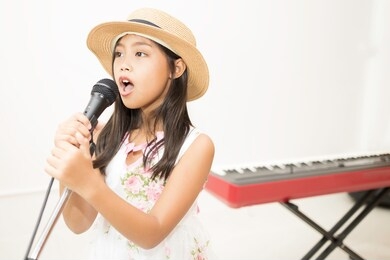 a cute, elementary school girl in asia is singing a song in the music classroom.