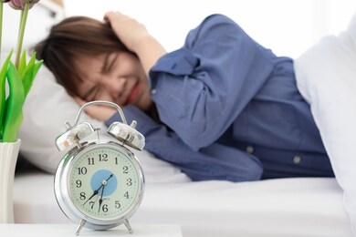 lazy young asian woman sleeping on white bed and turn off alarm clock wake up in morning.she don't want wake up.