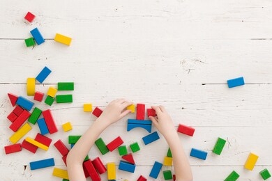 baby boy or girl play with colorful bricks on a white wooden table. top view on wooden colorful bricks on a wooden background. school, education and learning concept.