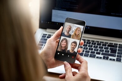 woman in video conference with a group of people. young business woman having a video chat with coworkers on her mobile phone. woman in her workplace with smartphone in her hands.