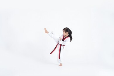 asian kid taekwondo kicking in white studio 