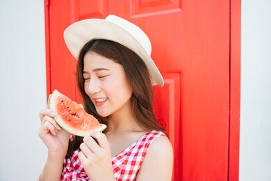 beautiful young asian woman in summer vacation holding slice of sweet watermelon over red door.
